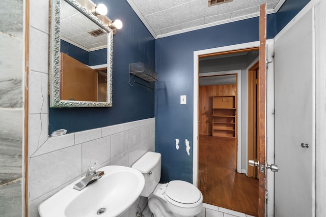 bathroom featuring toilet, tile walls, tile patterned floors, ornamental molding, and sink