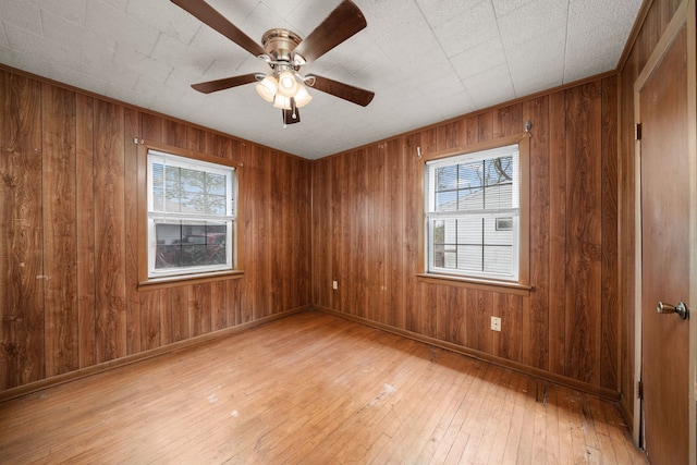 spare room featuring a healthy amount of sunlight, ceiling fan, light hardwood / wood-style flooring, and wood walls