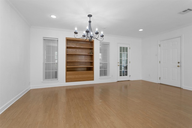 empty room featuring an inviting chandelier, built in features, ornamental molding, and light hardwood / wood-style floors