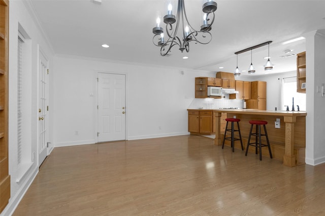 kitchen with kitchen peninsula, light hardwood / wood-style floors, a breakfast bar, backsplash, and ornamental molding