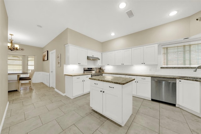 kitchen with dark stone countertops, appliances with stainless steel finishes, a center island, white cabinets, and sink