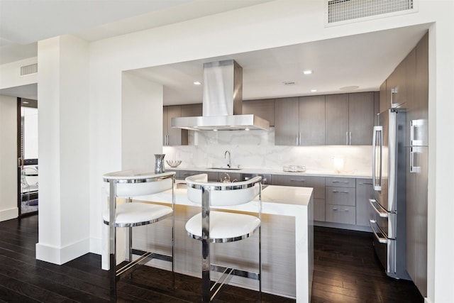 kitchen featuring island exhaust hood, stainless steel refrigerator, dark hardwood / wood-style flooring, a kitchen bar, and backsplash