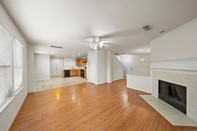 unfurnished living room with ceiling fan with notable chandelier, a tiled fireplace, and light wood-type flooring