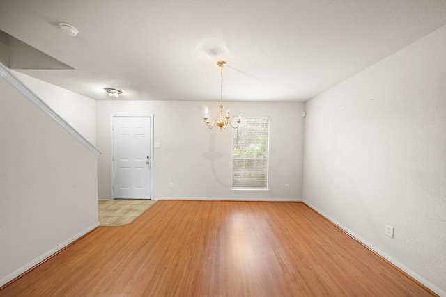 unfurnished room featuring a notable chandelier and light wood-type flooring