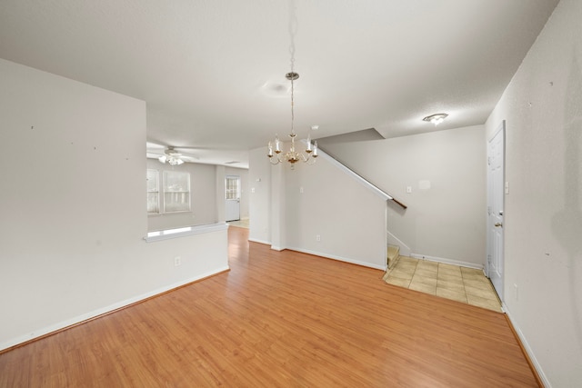 unfurnished living room with ceiling fan with notable chandelier and light hardwood / wood-style floors