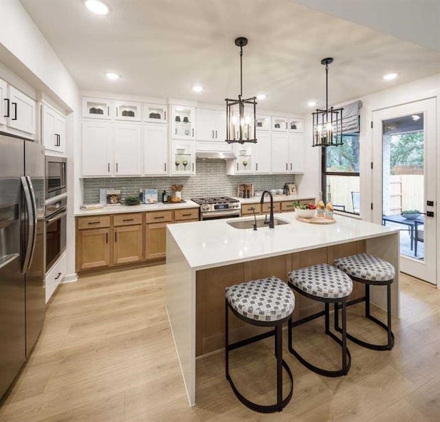 kitchen with pendant lighting, an island with sink, white cabinets, appliances with stainless steel finishes, and sink