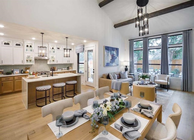 dining space with sink, a notable chandelier, light hardwood / wood-style floors, and vaulted ceiling with beams