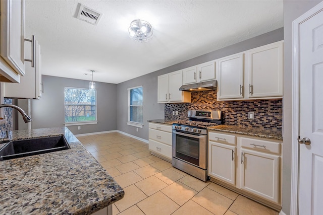 kitchen featuring stainless steel gas stove, backsplash, white cabinets, dark stone countertops, and sink