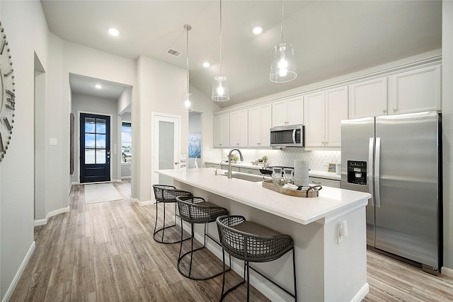 kitchen featuring stainless steel appliances, a center island with sink, white cabinetry, and hanging light fixtures