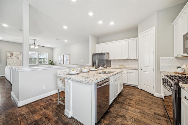 kitchen featuring an island with sink, appliances with stainless steel finishes, white cabinets, and decorative backsplash