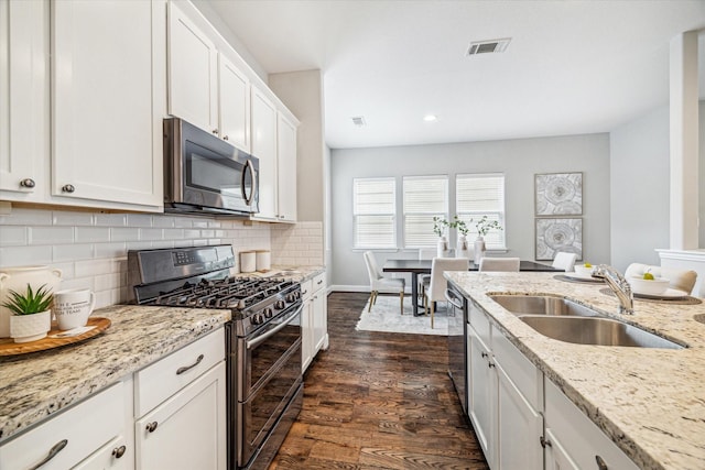 kitchen with sink, appliances with stainless steel finishes, white cabinets, light stone countertops, and dark wood-type flooring