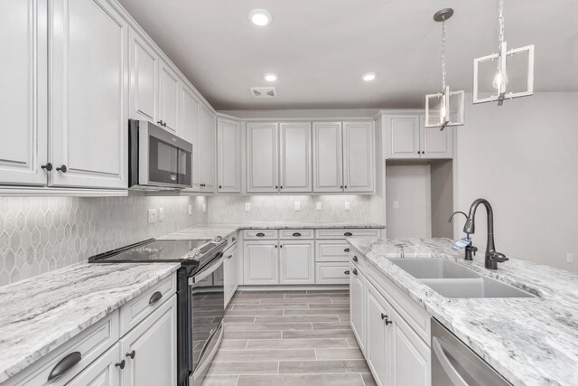 kitchen with sink, white cabinets, light stone counters, pendant lighting, and appliances with stainless steel finishes