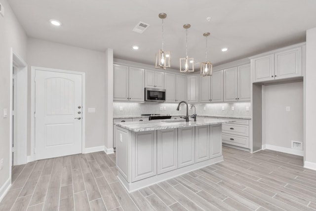 kitchen featuring light stone countertops, pendant lighting, a kitchen island with sink, backsplash, and sink