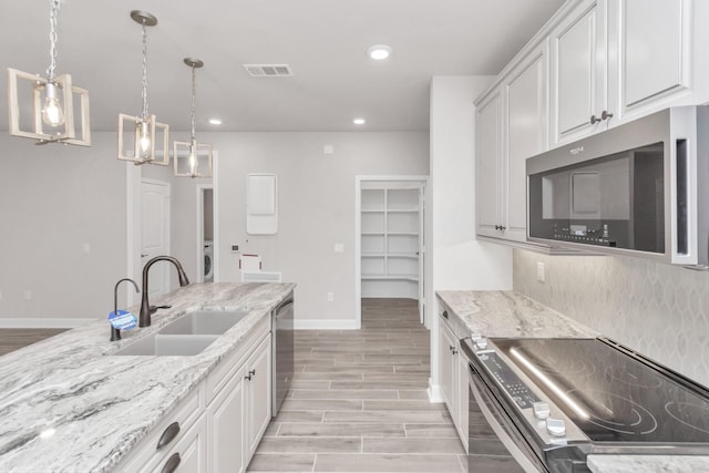 kitchen with appliances with stainless steel finishes, hanging light fixtures, sink, white cabinetry, and backsplash