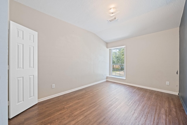 empty room with a textured ceiling, dark hardwood / wood-style flooring, and vaulted ceiling