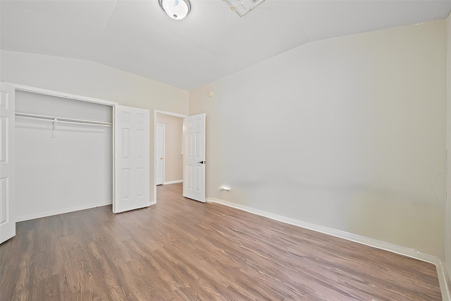 unfurnished bedroom featuring vaulted ceiling, a closet, and hardwood / wood-style flooring