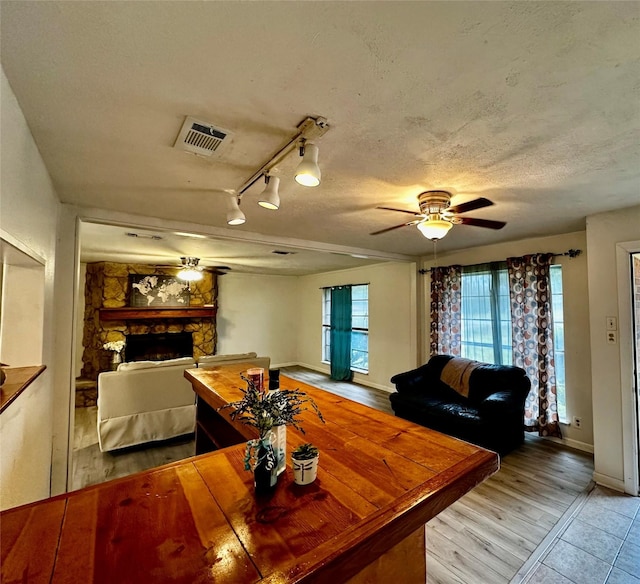 dining room featuring a textured ceiling, light wood-type flooring, rail lighting, ceiling fan, and a stone fireplace