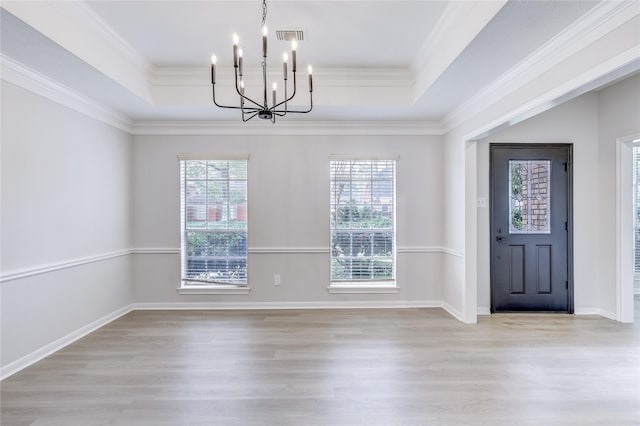 unfurnished dining area featuring ornamental molding, light hardwood / wood-style flooring, a chandelier, and a tray ceiling