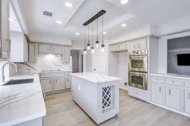 kitchen with hanging light fixtures, stainless steel double oven, a kitchen island, a tray ceiling, and sink