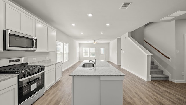 kitchen with sink, white cabinets, light stone counters, a kitchen island with sink, and appliances with stainless steel finishes