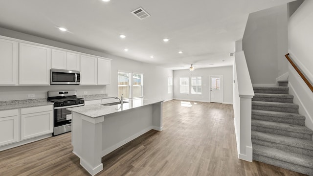 kitchen with ceiling fan, stainless steel appliances, white cabinets, and a center island with sink