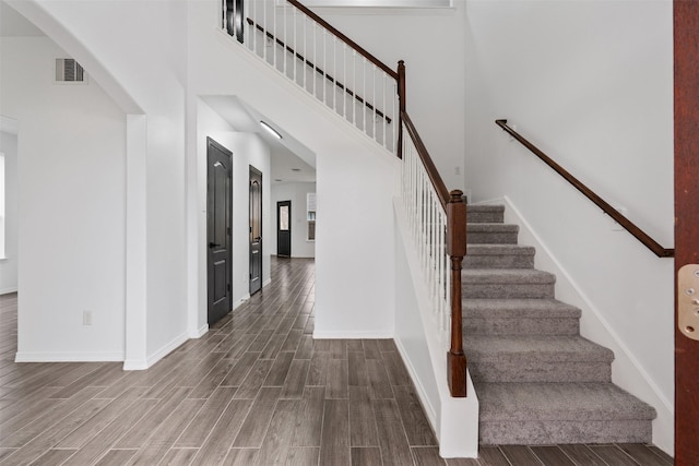 stairs featuring arched walkways, visible vents, a towering ceiling, wood tiled floor, and baseboards