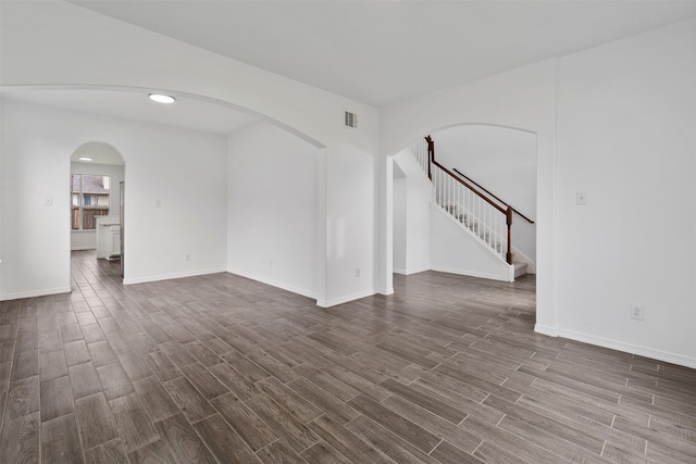 empty room featuring arched walkways, dark wood-type flooring, visible vents, baseboards, and stairs