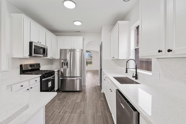 kitchen with appliances with stainless steel finishes, white cabinetry, a sink, and backsplash