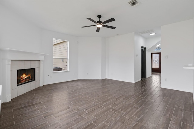 unfurnished living room featuring a tile fireplace, visible vents, dark wood finished floors, and ceiling fan