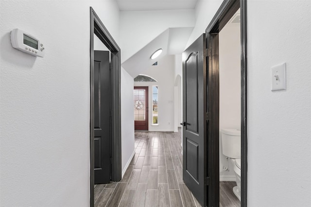 hall featuring wood tiled floor, arched walkways, and baseboards