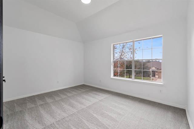 carpeted empty room featuring vaulted ceiling and baseboards