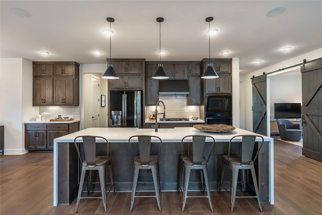 kitchen featuring a barn door, black appliances, dark hardwood / wood-style flooring, decorative light fixtures, and backsplash