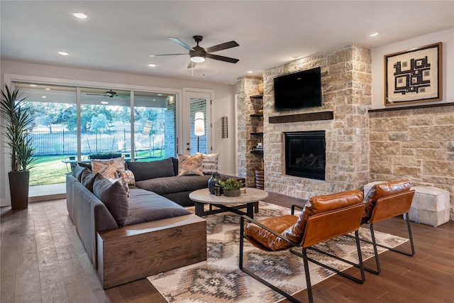 living room featuring ceiling fan, a stone fireplace, and hardwood / wood-style flooring