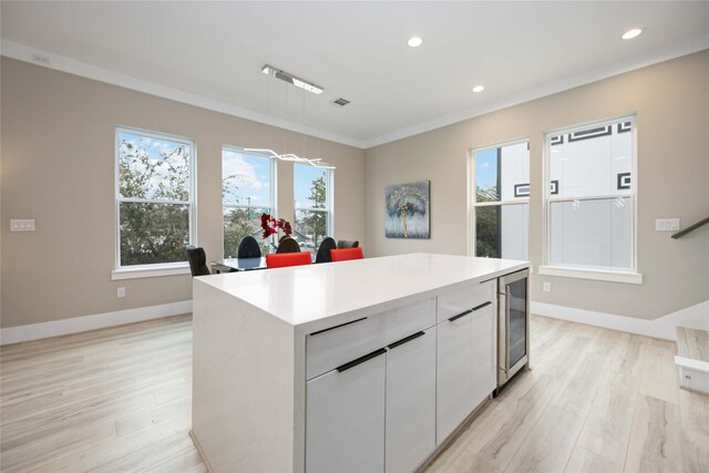 kitchen featuring a center island, decorative light fixtures, wine cooler, plenty of natural light, and white cabinetry