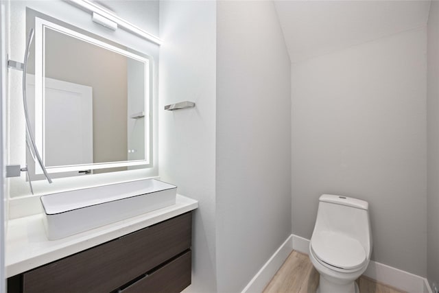 bathroom with hardwood / wood-style floors, vaulted ceiling, vanity, and toilet