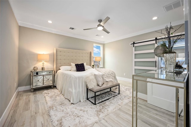 bedroom with ornamental molding, ceiling fan, a barn door, and hardwood / wood-style floors