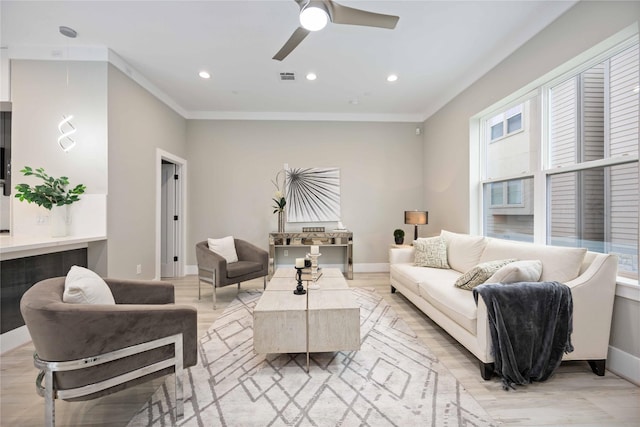 living room featuring ceiling fan, crown molding, light wood-type flooring, and a wealth of natural light