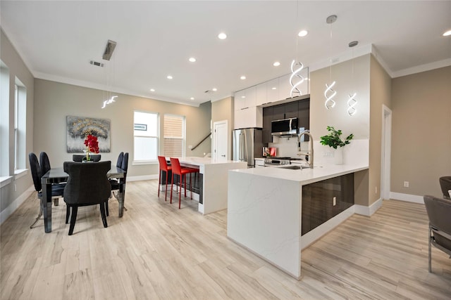 kitchen featuring sink, a kitchen bar, light hardwood / wood-style floors, hanging light fixtures, and appliances with stainless steel finishes