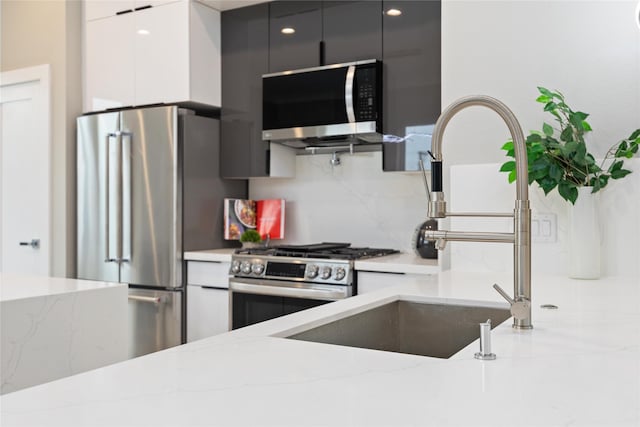 kitchen with light stone countertops, sink, backsplash, and appliances with stainless steel finishes