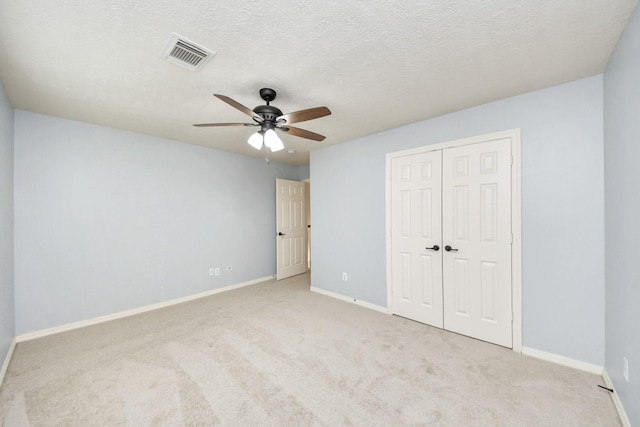 unfurnished bedroom with a textured ceiling, ceiling fan, a closet, and light carpet