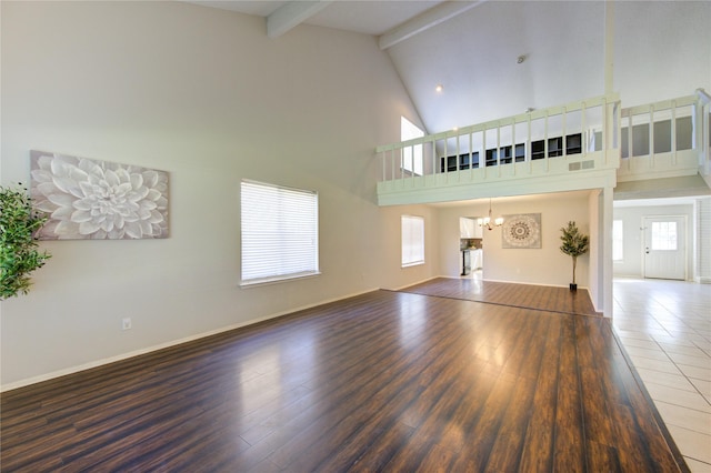 unfurnished living room with a notable chandelier, beam ceiling, hardwood / wood-style floors, and high vaulted ceiling