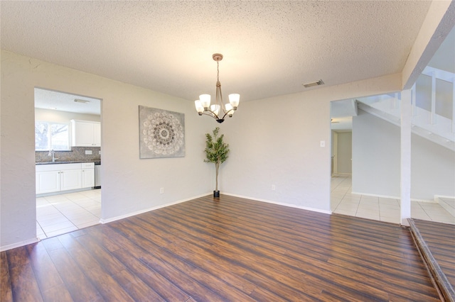 spare room featuring a notable chandelier, sink, a textured ceiling, and light hardwood / wood-style flooring