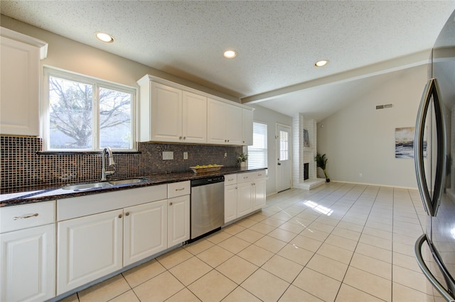 kitchen with appliances with stainless steel finishes, light tile patterned flooring, lofted ceiling, white cabinets, and sink