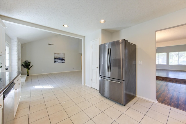 kitchen with a textured ceiling, appliances with stainless steel finishes, white cabinetry, vaulted ceiling, and light tile patterned floors