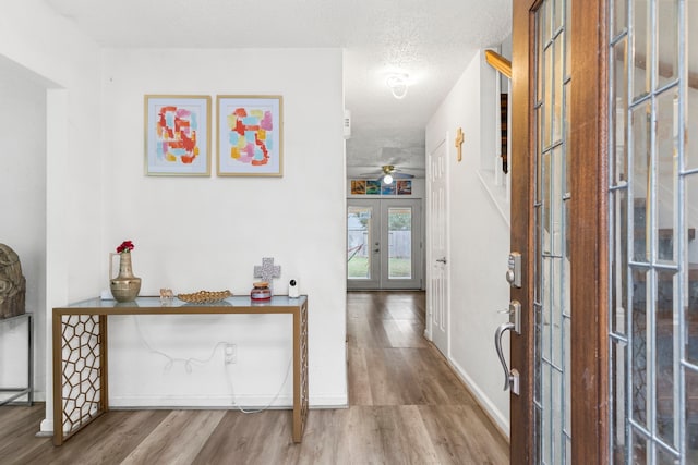 corridor with french doors, a textured ceiling, and hardwood / wood-style flooring