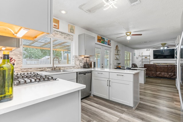 kitchen featuring sink, a textured ceiling, gas cooktop, kitchen peninsula, and stainless steel dishwasher