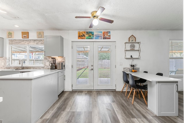 kitchen featuring kitchen peninsula, a textured ceiling, french doors, light wood-type flooring, and backsplash