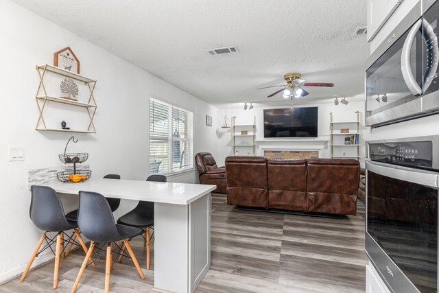 kitchen with a textured ceiling, dark hardwood / wood-style floors, stainless steel appliances, ceiling fan, and a kitchen breakfast bar