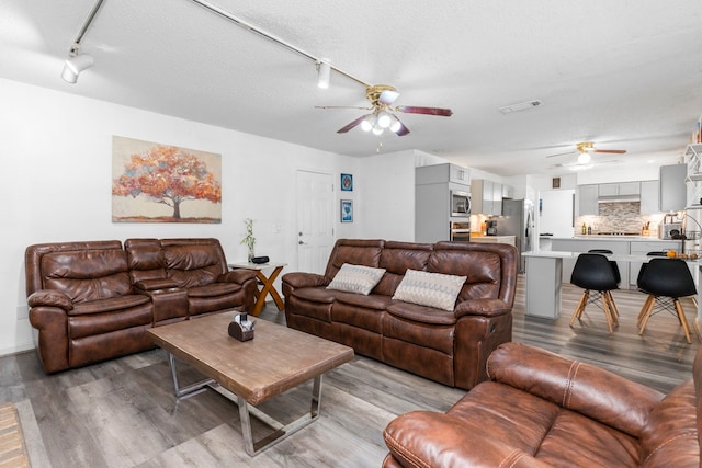 living room with a textured ceiling, rail lighting, ceiling fan, and light hardwood / wood-style flooring