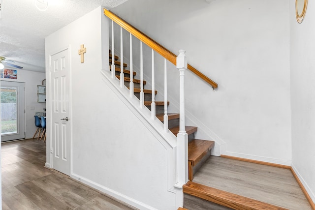 stairway with a textured ceiling, ceiling fan, and hardwood / wood-style flooring